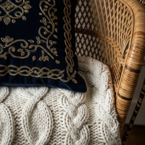 close-up of layered vintage textiles – a velvet pillow, a chunky knit blanket, and a woven rattan chair